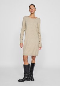 Cremfarbene Strickkleid mit langen Ärmeln und geripptem Saum. Kombiniert mit knielangen schwarzen Lederstiefeln mit Schnallen und einer runden Zehe.