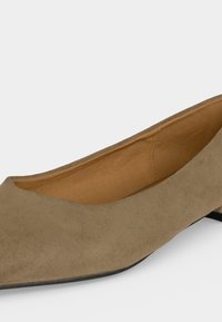 Gros plan sur une chaussure plate en daim beige avec un petit talon et une pointe arrondie légèrement pointue sur fond blanc.