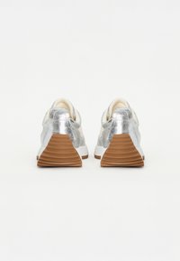 Silberne, metallische Sneaker mit strukturiertem Finish, weißer Sohle und braunem Profil. Sie verfügen über eine glatte, abgerundete Ferse und einen gepolsterten Kragen.