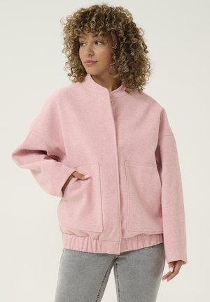 Pink oversized jacket with a high collar, two front pockets, and ribbed hem. Fabric has a soft texture with a subtle herringbone pattern.