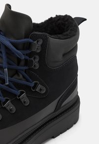 Black hiking boot with a smooth leather upper, blue laces, and metal eyelets. Features a thick rubber sole and a soft fleece lining.