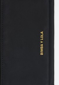 Black nylon bag with gold text "BIMBA Y LOLA." Features a smooth texture and clean lines, showcasing minimalist design elements.