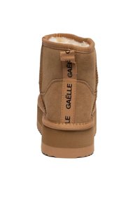Stivaletto alla caviglia in suede beige con interno morbido, suola piatta e linguetta posteriore con logo. Finitura liscia e design semplice.