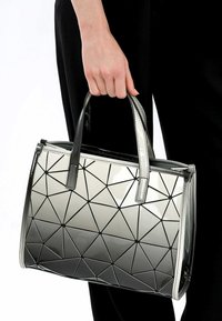Czarna i biała torebka z geometrycznym wzorem w trójkąty, błyszczący materiał, dwa uchwyty i zamek błyskawiczny. Udekorowana małymi czarnymi akcentami.