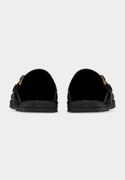 Vue arrière de mocassins noirs en cuir à enfiler avec accessoires dorés et semelle cousue sur fond blanc.