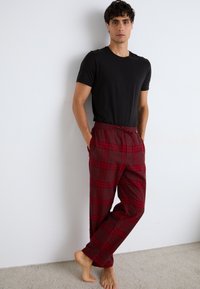 Pantalons de pyjama à carreaux rouges avec taille élastique et poches latérales, associés à un t-shirt noir à manches courtes. Texture de tissu douce.