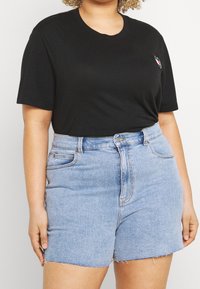 Sort bomulds T-shirt med korte ærmer og rund halsudskæring, parret med lyseblå denim shorts med frynset kant og forlommer.