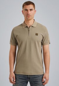 Khaki poloshirt met ritssluiting op de kraag, korte mouwen, geborduurd logo op de borst, rechte zoom en zijaccent. Glad katoen. 