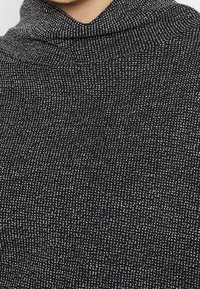 Tessuto a maglia nera con un motivo testurizzato, caratterizzato da un collo drappeggiato. Il tessuto ha una leggera lucentezza e un design a maglia fitta.
