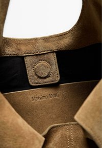 Interno in suede marrone di un indumento, con chiusura a pulsante a scatto e branding in rilievo "Massimo Dutti" su uno sfondo di tessuto morbido.