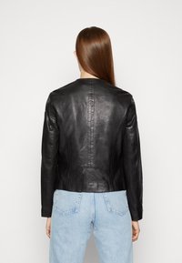 Svart skinnjacka med en figursydd design, med rund halslinning, långa ärmar och slät yta. Anmärkningsvärd sömnadsdetalj på ryggen.