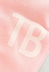 Roza pamučna tkanina s velikim, teksturiranim bijelim logotipom s natpisom "TB" i "by Ted Baker". Glatki, lagani materijal.