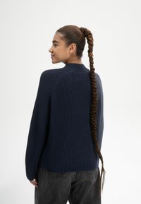 Marineblaues, geripptes Strickpullover mit hohem Kragen, langen Ärmeln und lockerer Passform. Trägt dazu eine dunkelgraue Hose.