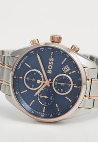 Orologio in acciaio inox argentato con quadrante blu scuro, accenti in oro rosa, tre sottocenti e una finestra per la data, dotato di una lunetta tachimetrica.