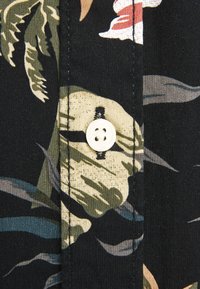 Camicia in tessuto a maniche corte con sfondo nero, foglie verdi e beige, fiori rossi e un bottone bianco sul colletto.