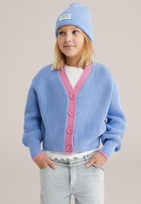 Cardigan azzurro chiaro lavorato a maglia con scollo a V rosa e bottoni. Indossato sopra una camicia bianca, abbinato a jeans in denim chiaro. Texture morbida e vestibilità comoda.