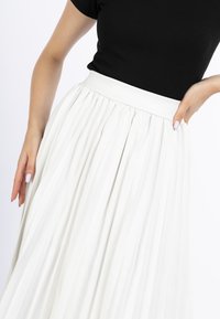Witte geplooide rok met een gladde tailleband, voorzien van verticale plooien over de hele lengte. De stof lijkt lichtgewicht met een zachte textuur.