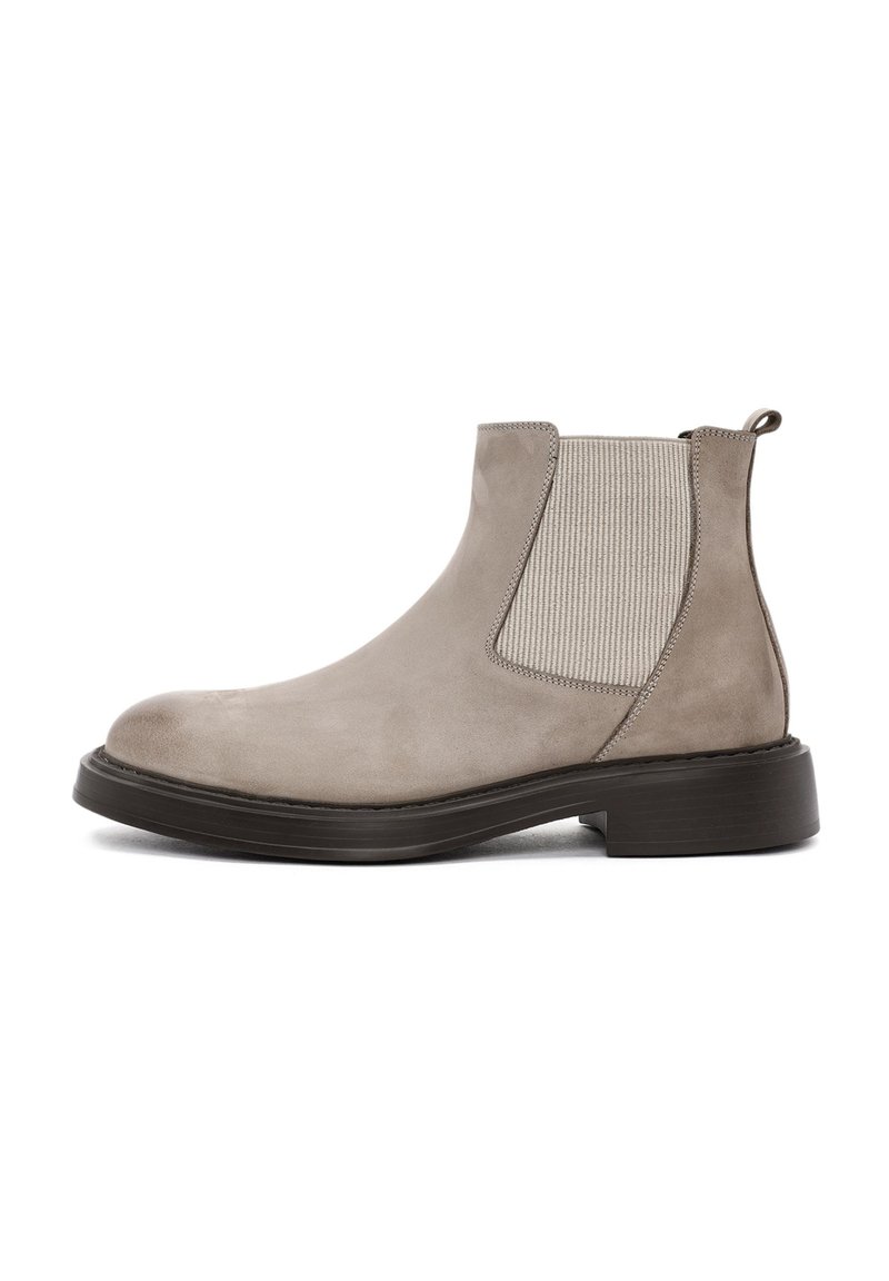 Botas Chelsea de ante gris claro con paneles laterales elásticos, puntera redondeada y suela de goma negra. Cuenta con una lengüeta trasera para facilitar su colocación.
