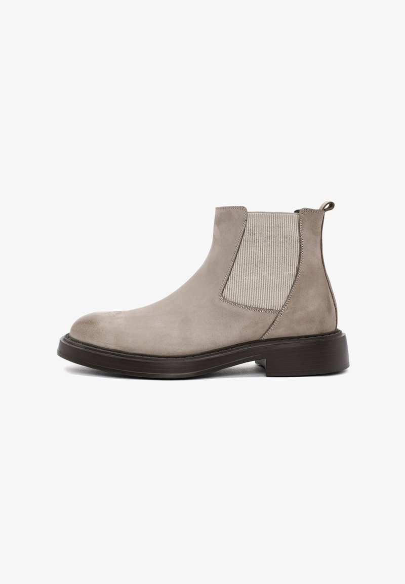 Botas Chelsea de ante gris claro con paneles laterales elásticos, puntera redondeada y suela de goma negra. Cuenta con una lengüeta trasera para facilitar su colocación.