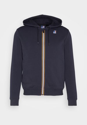 Sudadera con capucha azul marino con cremallera, ribete a rayas en la cremallera, bolsillos delanteros tipo canguro, capucha con cordón ajustable y pequeño logo en el pecho izquierdo.