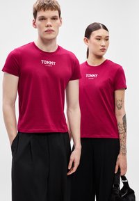 Bordó trička s krátkými rukávy, s bílým logem "TOMMY JEANS" na hrudi. Vyrobená z bavlny, kombinovaná s černými kalhotami.