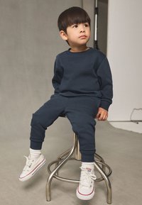 Sweat-shirt et pantalon bleu marine en matière douce, avec poignets côtelés, assortis à des baskets blanches ornées d'accentuations rouges et de semelles en caoutchouc.