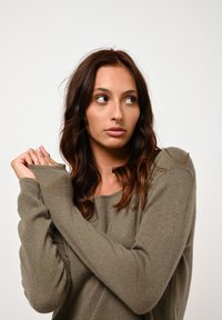 Maglione verde oliva a maniche lunghe realizzato in tessuto morbido e testurizzato, con una vestibilità rilassata e scollatura rotonda. Nessun motivo visibile o accessorio.
