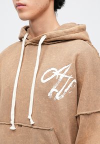 Rudi džemperiai su baltomis raištelėmis ir priekiu kišenėje. Yra dėvėtas apatinis kraštas ir baltas grafikos logotipas ant krūtinės. Minkšta, tekstūruota medžiaga.