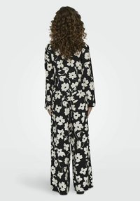 Blumen-Overall in Schwarz und Weiß mit langen Ärmeln, weit geschnittenem Bein und einem strukturierten Stoff mit einem auffälligen Blumenmuster.