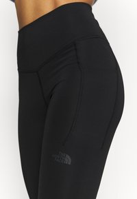 Zbliżenie czarnych legginsów z wysokim stanem, z boczną kieszenią i logo The North Face na udzie.