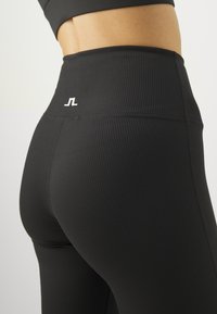 Svarta ribbade leggings med hög midja och en vit logotyp på höften. Tyget verkar elastiskt och har en slät textur.