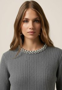 Šedý žebrovaný svetr s dekorativním výstřihem zdobeným perlovými akcenty, představující měkkou texturu a přiléhavý střih.