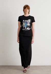 Black t-shirt featuring a graphic of two figures and a dog, paired with a long black skirt and black strappy sandals. Simple, unembellished design.