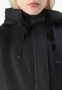 Black hooded jacket featuring a smooth, matte finish, with adjustable black straps and a high collar design.