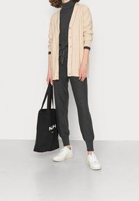 Beżowy kardigan, szary golf i dopasowane joggery. Białe trampki z teksturowaną podeszwą. Czarna torba na ramię z białym logo. Prosty i przytulny wygląd.