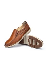 Zapatos marrones de cuero tipo slip-on con un acabado suave, paneles laterales elásticos y una suela de goma beige con un patrón de agarre texturizado.