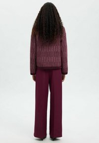 Bordowy sweterek z teksturowanymi pionowymi paskami, w połączeniu z spodniami o wysokim stanie i szerokich nogawkach w pasującym odcieniu bordowym. Gładkie wykończenie materiału.