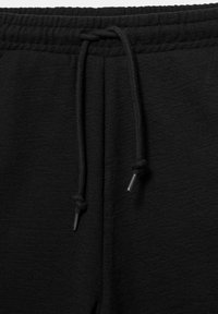 Ceinture élastique noire avec cordon noué sur un tissu texturé, probablement un pantalon de survêtement ou un jogging.