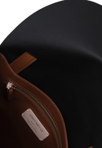 Intérieur d'un sac à main en cuir noir avec une poche zippée marron, étiquetée "Coccinelle", mettant en avant une texture lisse et un design épuré.