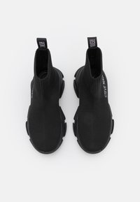 Bottes noires à la cheville avec une tige en tricot extensible et une semelle en caoutchouc, équipées d'une languette de tirage et d'un détail de marque minimal sur le côté.