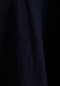 Tissu tissé bleu foncé avec une texture subtile et des plis verticaux sur fond noir.