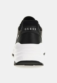 Sneaker nera con tomaia in pelle liscia, intersuola bianca e suola nera. Il logo "GUESS" è visibile in bianco nella sezione del tallone.