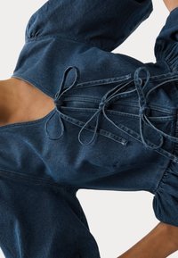 Donkerdenim top met pofmouwen, vetersluiting met strikjes langs de halslijn, getailleerde taille voor een aansluitende look en een zachte textuur.