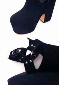 Gli stivali alla caviglia in suede nero con piattaforma presentano una punta arrotondata, un alto tacco a blocco e una cintura regolabile con dettagli metallici. Fodera interna liscia.