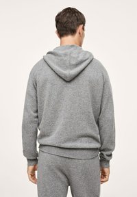 Szara bluza z kapturem wykonana z miękkiego, teksturowanego materiału. Posiada sznurek w kapturze, ściągacze na mankietach i w pasie. Noszona z dopasowanymi szarymi spodniami.