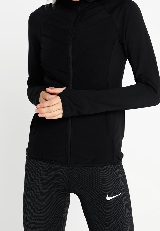 Black zip-up athletic jacket with a fitted design and textured paneling, paired with black and gray patterned leggings featuring a white logo.