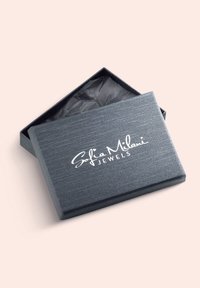 Grå rektangulär smyckesask med en strukturerad yta, med en vit logotyp "Sofia Milani JEWELS" på locket, något öppen för att avslöja svart silkespapper inuti.