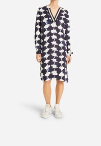 Šaty s dlouhým rukávem v námořnické a bílé geometrické vzory, s výstřihem do V a kontrastním lemem, a uvolněný střih, který sahá těsně nad kolena.