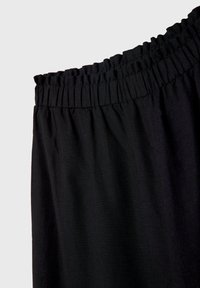 Gros plan de la ceinture élastique noire d'un pantalon en tissu doux et ample sur fond uni.