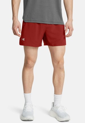 Mand iført røde atletikshorts, hvide sokker og hvide løbesko, stående på en hvid baggrund.